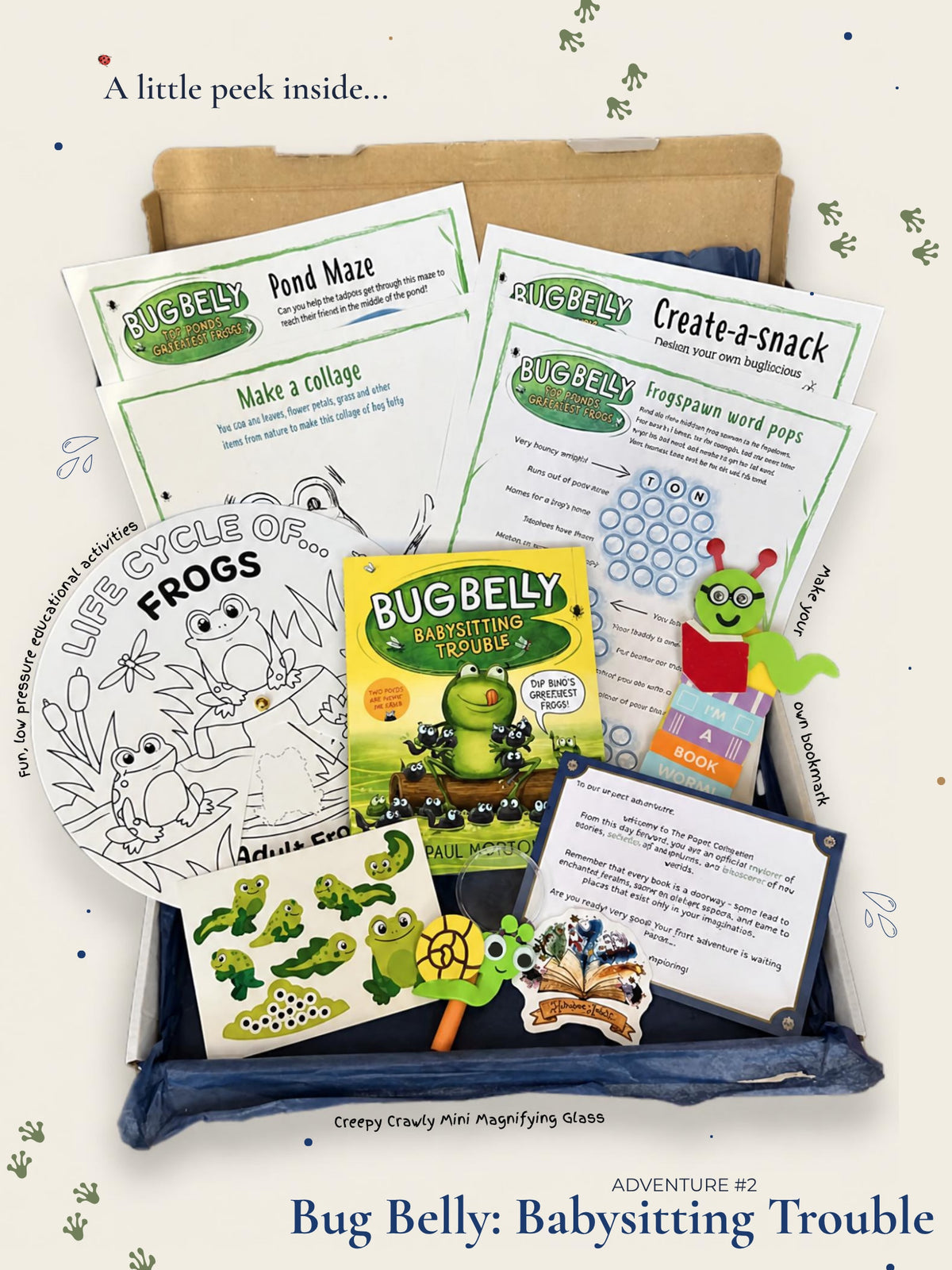 A children's activity kit labeled 'Bug Belly: Babysitting Trouble' arranged in a cardboard box with a blue fabric liner. Visible contents include printed worksheets, a coloring page, a book, a magnifying glass, and small frog-themed accessories.